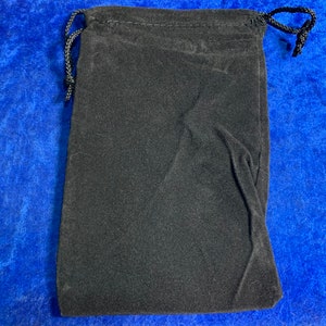 May include: A black velvet drawstring bag. The bag is closed and lying flat on a blue surface.