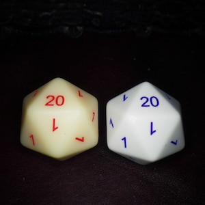 Puede incluir: Dos dados poliédricos de veinte caras, uno crema y otro blanco. El dado crema tiene números rojos, el dado blanco números azules. Ambos dados muestran los números 1 y 20. Ideales para juegos de mesa.
