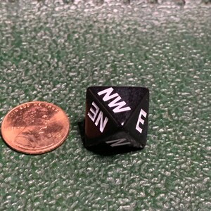 May include: A black, six-sided dice with white letters showing the directions: NW, NE, E, N.