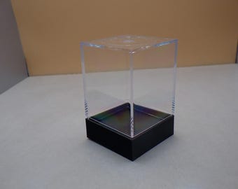 May include: A clear acrylic cube display case with a black base. The case is empty and ready to display a collectible item.