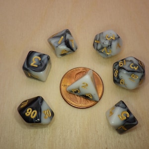 May include: Set of seven black and white marbled dice with gold numbers. The dice are arranged in a circle around a penny.