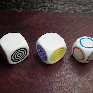 May include: Three white dice with different colored rings and spiral patterns. The dice have a black, yellow, and blue ring.