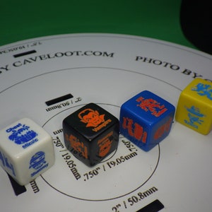 May include: Four different colored dice with various symbols and text. The dice are white, black, blue, and yellow. The text on the dice includes "Chest", "Mummy", "Vampire", "Sanct", and "Miralc".