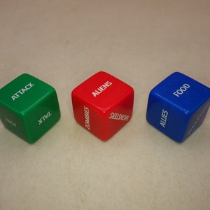 May include: Three dice with different colors and words on each side. The green die has the words "Attack", "Talk", "Back", "Run", "Hide", and "Help". The red die has the words "Aliens", "Zombies", "Monsters", "Food", "Water", and "Shelter". The blue die has the words "Food", "Allies", "Weapons", "Medicine", "Tools", and "Supplies".