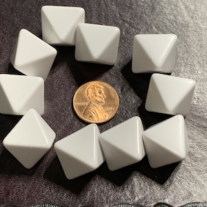 May include: Ten white pyramid-shaped dice, arranged in a circle around a copper penny. The penny is dated 2017.