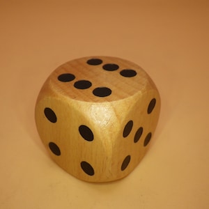 May include: A wooden dice with black dots on each side. The dice is made of light brown wood and has a natural finish.