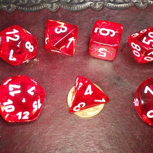 May include: Set of seven red dice with white numbers. The dice are a d4, d6, d8, d10, d12, and two d20s.