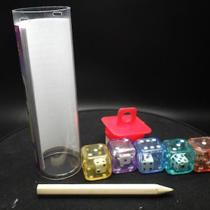 May include: A set of six clear dice with white dots, each die is a different color: yellow, purple, blue, green, orange, and red. The dice are in a row on a black surface. There is a small red plastic container with a handle and a clear plastic tube with a white label.