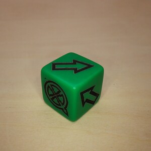 Puede incluir: Un dado verde de seis caras con marcas negras. El dado tiene una flecha apuntando hacia arriba en un lado, una flecha apuntando hacia arriba en otro lado y un c&iacute;rculo con una cruz dentro en un tercer lado.