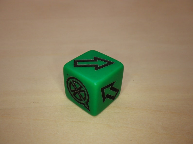 Puede incluir: Un dado verde de seis caras con marcas negras. El dado tiene una flecha apuntando hacia arriba en un lado, una flecha apuntando hacia arriba en otro lado y un c&iacute;rculo con una cruz dentro en un tercer lado.