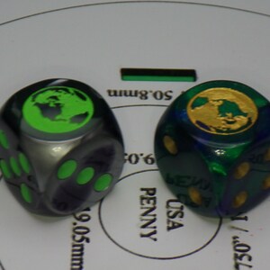 May include: Two dice with a green and gold globe design. The dice are black and blue with green and gold dots. The dice are 1.96 inches in diameter.