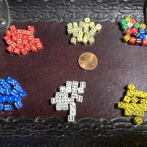 May include: A collection of dice in various colors, including red, blue, white, yellow, and black, are scattered on a brown leather surface. The dice are all standard six-sided dice.
