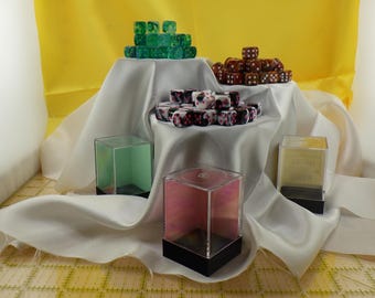 May include: Four clear acrylic display boxes with black bases, each containing a different set of dice. The dice are green, brown, white with pink accents, and white with black accents.