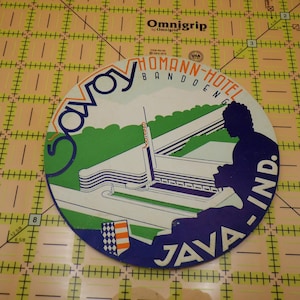May include: A circular vintage travel souvenir featuring the Savoy Homann Hotel in Bandung, Java. The design includes the hotel's facade, a silhouette, and the text "Savoy Homann Hotel Bandung Java Ind." in blue, green, and white.