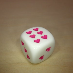 May include: A white dice with pink hearts on each side.