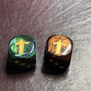 May include: Two dice with a gold figure on each side. One die is green with black spots and the other is brown with black spots.