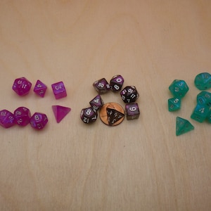 May include: A set of 15 iridescent dice in purple, green, and black colors. The dice are numbered 1 through 10, and 4, 6, 8, 10, and 12 sided.