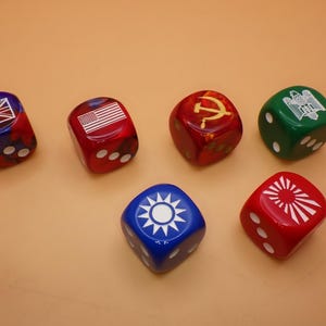 May include: Six six-sided dice featuring various national and political symbols. The dice are colored red, blue, and green, with white pips on the sides. Symbols include the Union Jack, the American flag, a hammer and sickle, an eagle, a sunburst, and a star.