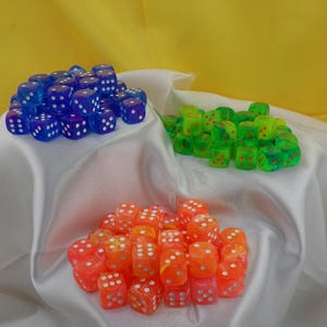 May include: Three piles of dice on a white fabric surface. The dice are translucent and come in blue, green, and orange colors. The dice have white dots on each side.
