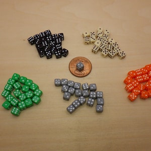 May include: Assortment of dice in various colors, including black, green, gray, orange, and white. The dice are arranged in a circle on a wooden surface.