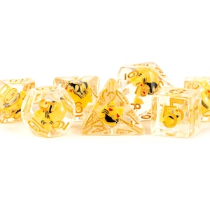 May include: A set of seven translucent yellow dice with black and gold accents. The dice are numbered 1 through 6 and feature a cartoon cat design.
