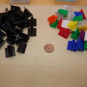 May include: A pile of black plastic game pieces and a pile of colorful plastic game pieces, including red, blue, green, orange, purple, and white. A penny is in the center of the image.