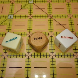 May include: Three dice with the words "PLATINUM", "SILVER", and "ELECTRUM" printed on them. The dice are white and wooden, and are arranged on a yellow grid.