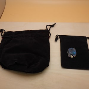 May include: Two black velvet drawstring bags, one larger than the other. The smaller bag contains a silver and blue iridescent dice with black dots.