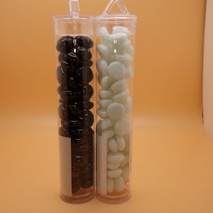 May include: Two clear glass tubes filled with small glass pebbles. One tube contains black pebbles and the other contains white pebbles.