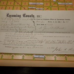 May include: An antique off-white legal document from Lycoming County dated 1867, featuring black cursive handwriting and printed text. The document is placed on a yellow grid mat with inch markings, showing a total width of approximately 10 inches.