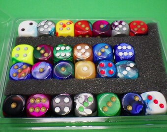 May include: A clear plastic box filled with 24 colorful dice. The dice are made of a translucent material with swirls of color and gold accents. The dice are arranged in two rows of 12.
