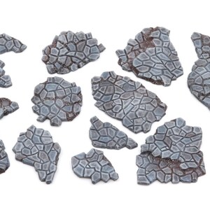 May include: A set of 12 grey and brown stone-like terrain pieces for tabletop gaming. The pieces are irregularly shaped and have a rough, textured surface.