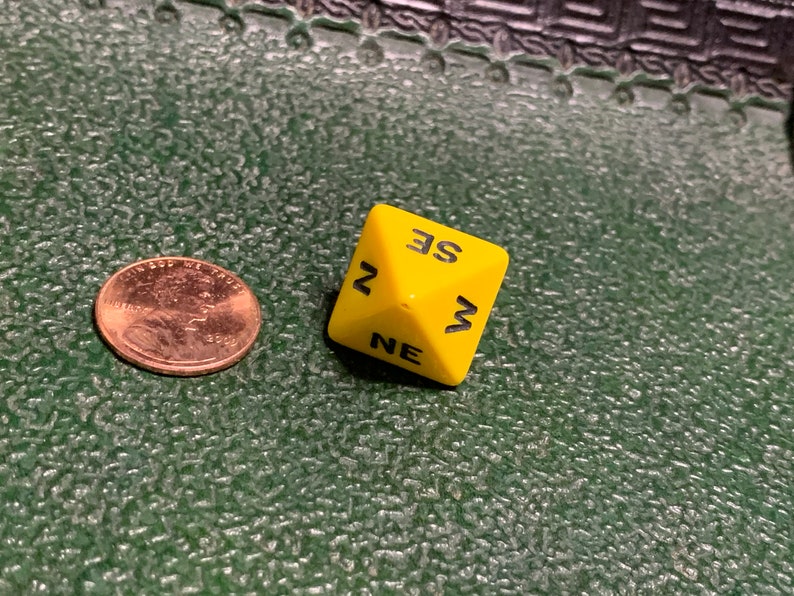 May include: A yellow six-sided die with black lettering. The die shows the letters "NE", "W", "SE", and "N".
