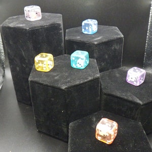 May include: Six clear dice with different colored tints displayed on black hexagonal platforms. The dice are clear and show white numbers. The colors of the dice are clear, yellow, blue, purple, orange, and pink.