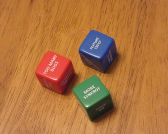 May include: Three dice with different colored backgrounds and white text. The red die says "Too Many Bugs", the blue die says "Feature Creep", and the green die says "More Synergy".