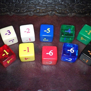 May include: A collection of ten multi-colored dice, each displaying different negative numbers and symbols. The dice are in various colors, including red, yellow, blue, and green, and are arranged on a dark brown surface.