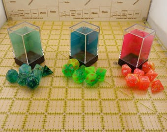 May include: Three clear plastic boxes containing sets of green, blue, and red dice. Each set of dice has a translucent, iridescent finish with white numbers.