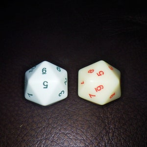 May include: Two twelve-sided dice. One die is white with green numbers, the other is off-white with red numbers. The dice are used for tabletop games and role-playing games. The dice are made of plastic.