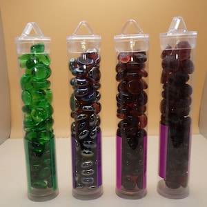 May include: Four clear plastic tubes filled with decorative glass pebbles. The tubes are labeled with different colors: green, iridescent, red, and black.