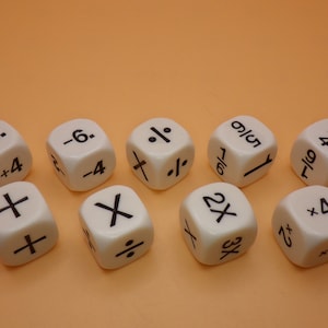 May include: Ten white dice with black markings. Each die has a different symbol or number combination, including plus signs, minus signs, division signs, multiplication signs, and percentages.