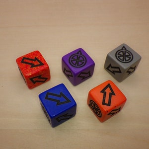 May include: Five dice with different colored backgrounds and black symbols. The dice are orange, purple, gray, blue, and orange. The symbols are arrows and a wheel.