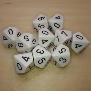 May include: A group of ten white dice with black numbers. The dice are scattered on a light brown wooden surface.