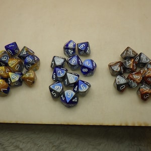 May include: Three sets of dice, each set in a different color. The first set is blue and gold, the second set is blue and silver, and the third set is brown and silver.