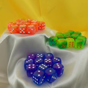 May include: A set of 18 dice in three colors: orange, green, and blue. Each die has white dots on the sides. The dice are arranged in three groups on a white satin surface.