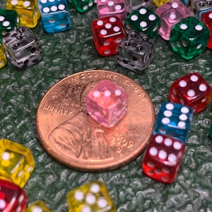 May include: A close-up of a collection of colorful, transparent dice with white dots. The dice are scattered on a green surface, with a penny in the center. The penny is dated 2009 and has the words "In God We Trust" and "Liberty" inscribed on it.