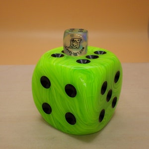May include: A green and black marbled dice with black dots on each side. A clear dice with black markings is on top of the green dice. The clear dice has the text "CAVELOO.COM" on one side.