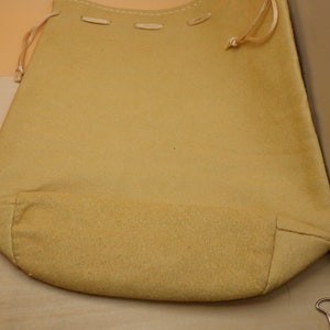 May include: A tan drawstring bag made of fabric with a gathered bottom. The bag has a simple design with no visible embellishments.