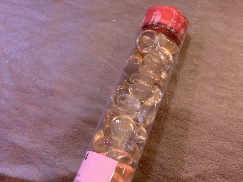 May include: A clear plastic tube filled with small, translucent, light amber-colored glass beads. The tube has a red lid and a pink label with the number "4" on it.