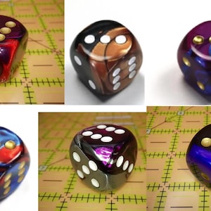 May include: A collection of six-sided dice featuring swirling, multi-colored resin patterns in shades of red, blue, purple, and black. Each die has rounded corners and recessed circular pips filled with either gold or white paint.