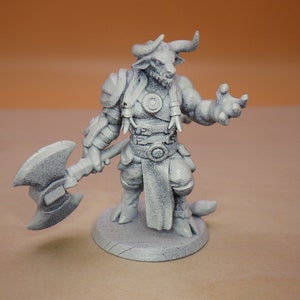 May include: A white painted miniature figurine of a minotaur warrior holding an axe. The figurine is standing on a round base.